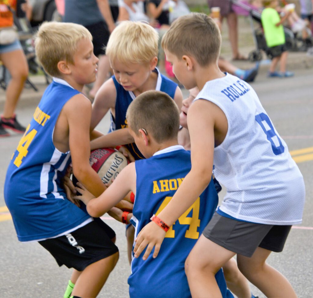 Four boys playing basketball outdoors, competing for the ball.