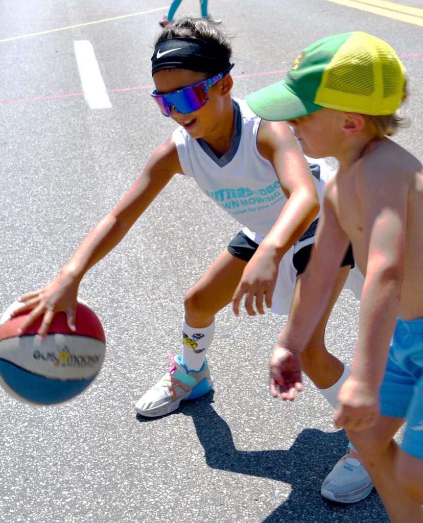 Two boys playing basketball outdoors on a sunny day.