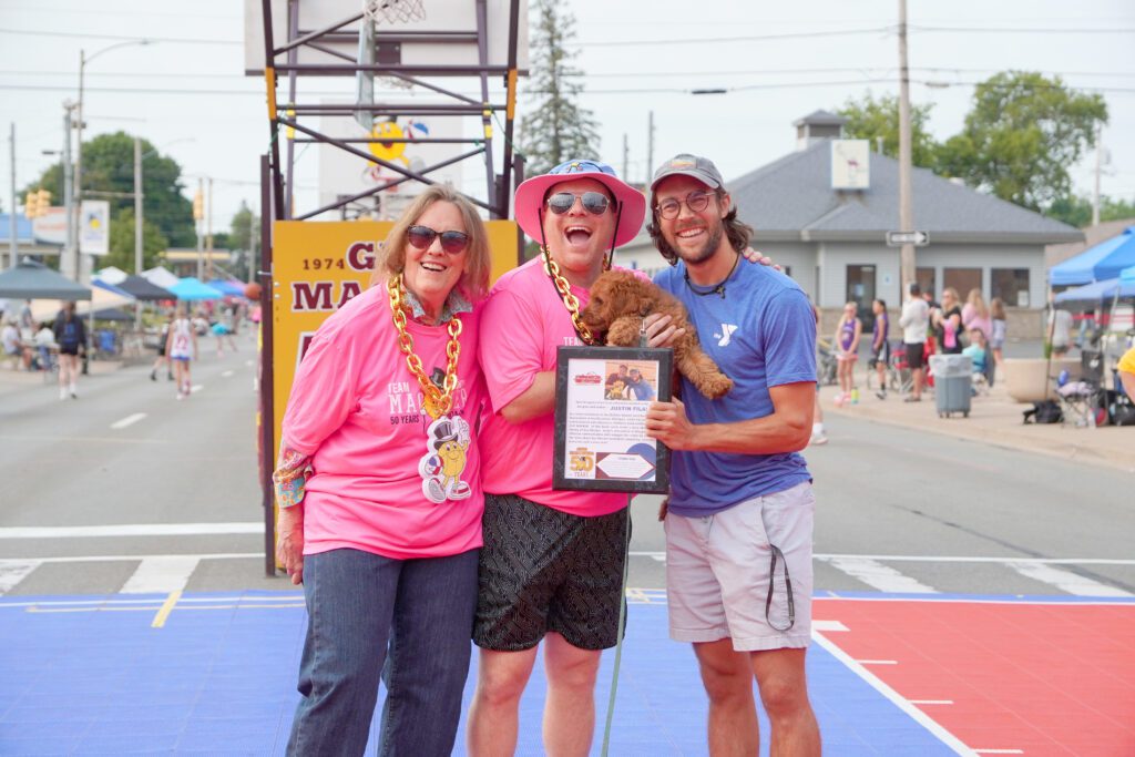 Three men smiling and holding a certificate at an outdoor event.