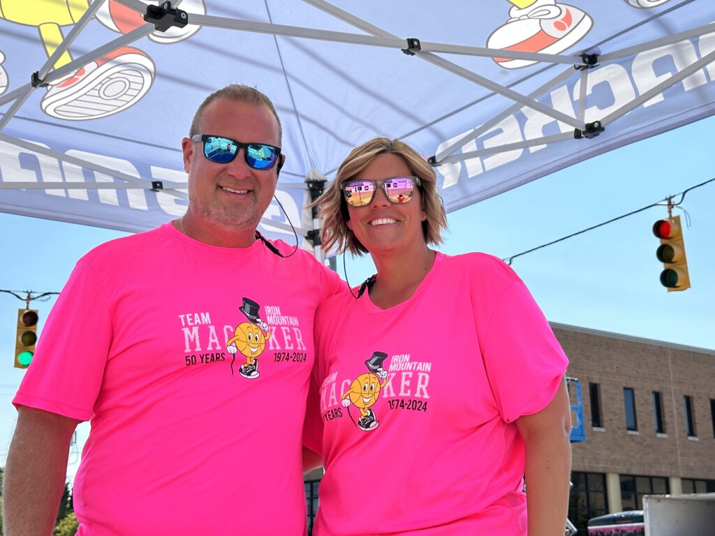 Couple wearing matching bright pink shirts and reflective sunglasses at an outdoor event.