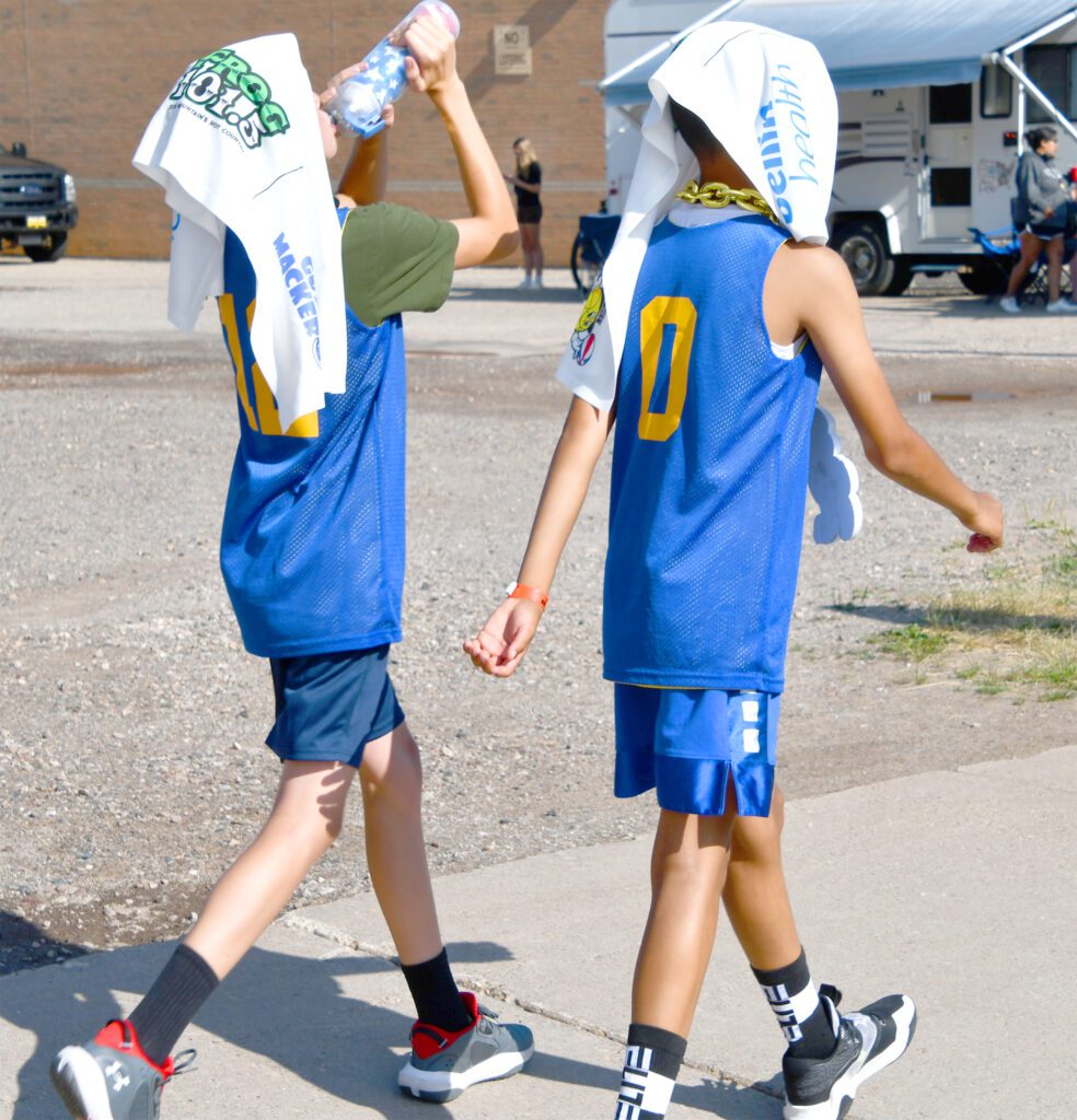 Two boys in blue sports uniforms walking with towels on their heads.